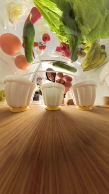 Bir adam yeşil jöleli bardağa uzanırken onu kırmızı bardağa tercih ettiği düşünülürse, buzdolabının içinden bakın. Yakın çekim, odaklanmış anı ahşap bir rafta yiyeceklerle yakalıyor..