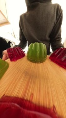 Renkli kırmızı ve yeşil jöle kalıplarının insan olarak sallanarak buzdolabına doğru taşındığını gösteren yakın plan bir perspektif. Kamera açısı dinamik bir şekilde birinci şahıstan üçüncü şahsa kayar..