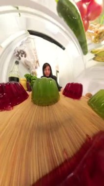 Buzdolabının içinden, bir adam sallanan kırmızı ve yeşil bir jöle tepsisi yerleştirir, yumuşak desenli jöleler rafta hafifçe sallanırken kapıyı kapatır..