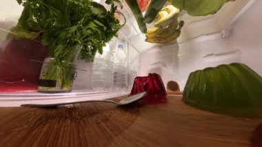 Buzdolabının içinde, dairesel bir manzara raflarda taze ürünlerle birlikte kırmızı ve yeşil ev yapımı jöleyi bir tepside yakalar. Yakın çekim parlak dokuları ve canlı renkleri vurgular.