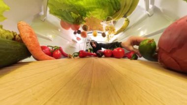 Buzdolabının içinden yakından bakınca raflarda salatalık, domates ve havuç gibi taze sebzeler düzenleyen bir adam görülüyor. Canlı renkler ve dokular vurgulandı.