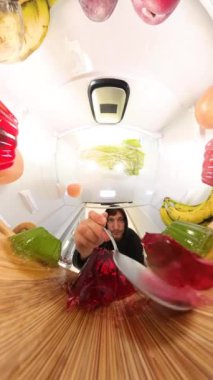 Dikey video. Buzdolabının içine geniş açılı bir bakış açısı, canlı meyve ve sebzelerle çevrili, jöle yiyen adamı çarpıcı bir şekilde yakalar..