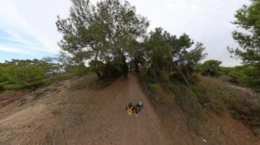 Kemerli ağaçların altında dar bir orman yolu, sırt çantalarıyla yan yana yürüyen bir erkek ve kadını gösteriyor, hava manzarası doğal uyumu yakalıyor..