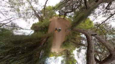 Ağaçlarla çevrili manzaralı bir orman yolunda yürüyen iki gezgin, küçük bir gezegen etkisine sahip havadan bir perspektiften yakalandılar.