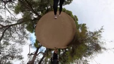 Parlak bir gökyüzünün altındaki canlı bir ormanla çevrili kumlu bir yolda yürüyen bir yürüyüşçünün ayaklarını gösteren küresel bir manzara..
