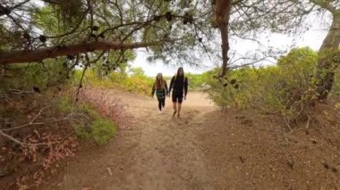 Bir erkek ve kadın, hareketlerini dinamik bir şekilde takip ederek, alçak açılı bir perspektifle orman arazisinde adımlarını yakalıyorlar..