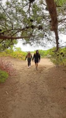 Dikey video. Bir erkek ve kadın, hareketlerini dinamik bir şekilde takip ederek, alçak açılı bir perspektifle orman arazisinde adımlarını yakalıyorlar..