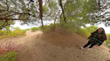 Bir erkek ve kadın ağaçların gölgesinde yürür, kamera arkalarından hareketlerini takip eder, orman zemininde ışığın ve gölgenin dinamik etkileşimini yakalar..