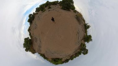 Küçük bir gezegen, bulutlu bir gökyüzünün altında bir sırt çantası taşıyan bir adam yüzeyinde yürürken döner ve eşsiz küresel bir perspektif yaratır..