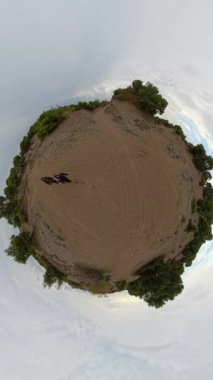 Dikey video. Küresel bir gezegen manzarası bulutlu bir gökyüzünün altında kumlu ovalarda yürüyen iki insanı gösteriyor. Gerçeküstü bir etki yaratıyor.