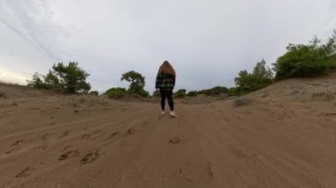 Düşük açılı bir çekim kumlu zeminde yokuş yukarı yürüyen bir kadını yakalıyor. Tırmanma hareketini ve çabasını vurgulamak.