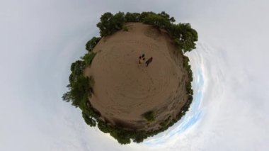 Arazinin genişliği ve insan varlığının küçüklüğü üzerine odaklanarak açık ve kumlu bir alanın ortasında iki gezginin küresel görüntüsü..