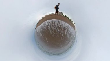 Bir çift kumlu bir sahil boyunca yürür ve hafif dalgalar kıyıya vurur. Küçük Gezegen etkisi küresel plajı ve çevreyi aydınlatır. Bulutlu gökyüzü ve serin hava manzarayı güzelleştiriyor.