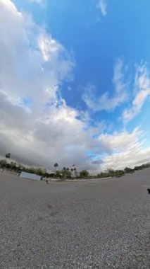 Dikey video. Dönen bir hava perspektifinden çekilen çakıl taşı plajının geniş açılı görüntüsü dalgaları, ufku ve dramatik gökyüzünü dinamik bir sahnede dağınık bulutlarla gösteriyor..