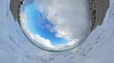 İç dalga perspektifi, deniz köpüğü ve dramatik bulutlu gökyüzü ile bir plajın dairesel panoramasını yaratarak, ufku eşsiz bir daldırıcı etkiyle yakalıyor..