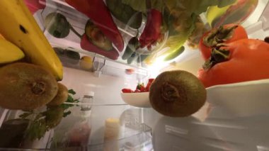 Buzdolabının içinde dönen bir kamera kapıyı açan ve canlı meyve ve sebzelerle çevrili bir kiviye uzanan bir adamı yakalar ve dinamik ve sürükleyici bir sahne yaratır..