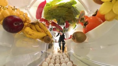 Doli zum efekti, rengarenk meyveler ve canlı ürünlerle çevrili buzdolabından salata için çeşitli sebzeler alan bir adamı parlak ve taze bir şekilde yakalar..