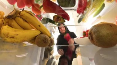 Yakın plan bakış açısı, taze ürünlerle çevrili buzdolabını açtıktan sonra et konteynırını inceleyen bir adamın sebzeler yerine eti seçme kararını sembolize ettiğini gösteriyor..