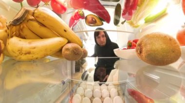 Buzdolabından alınmış renkli meyve ve sebzelerle çevrili bir et paketini inceleyen bir adam, vejetaryen seçeneklerine karşı görsel olarak bir seçim sunuyor..