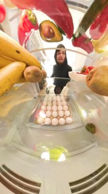 Dikey video. Buzdolabının içinde, bir adam taze ve canlı bir şekilde renkli ürünlerin arasında yakalanan sebzelerden uzaklaşırken verdiği kararı düşünen bir et paketi tutuyor..