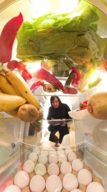 Dikey video. Buzdolabının içinden bir perspektif, kıyma paketini dikkatlice inceleyen bir adamı gösteriyor. Ama en sonunda onu renkli meyve ve sebzelerle çevrili bir şekilde içeride bırakıyor..