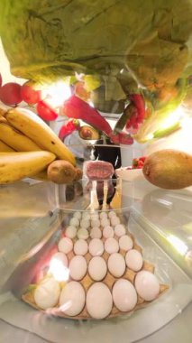 Dikey video. Dolly Zoom, buzdolabının içinden bir perspektif bir adamın kapıyı açıp canlı meyve ve sebzelerle çevrili bir paket kıyma paketini aldığı anı yakalar..