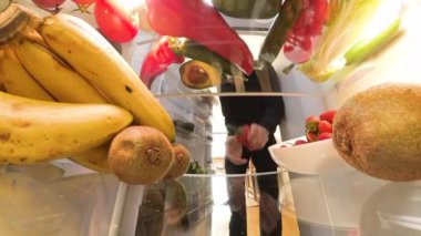 Buzdolabının içinden bir perspektif, canlı meyveler ve renkli ürünlerle çevrili canlı ve düzenli bir şekilde sebze ve yumurta almak isteyen bir adamı gösteriyor..