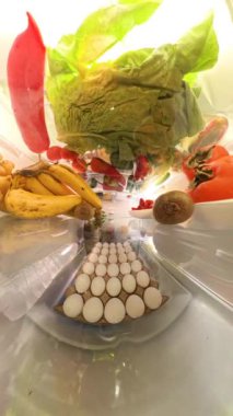 Dikey video. Buzdolabının geniş açılı yakın plan görüntülerinde taze meyve, sebze ve yumurtalar sergilenerek parlak bir ortamda canlı ve dinamik bir perspektif oluşturulur..