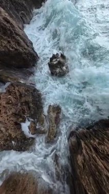 Dikey video. Su damlacıkları ve köpüklerin havada asılı kaldığı kayalık uçurumlara karşı dalgaların geniş açılı yavaş çekim gücü okyanusun ham enerjisini vurguluyor..