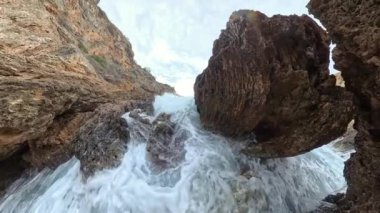 İki yüksek kaya oluşumu arasında çarpışan dalgaların yakın çekim çekimi yoğun kuvveti ve yüksek detay ile uçan su damlacıklarını yakalıyor..