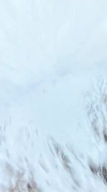 Dikey video. Keskin kayalıklara karşı köpüğe dönüşen bir dalganın yavaş çekim gücü, çarpmanın etkisiyle su damlacıkları ve çalkantılı paternler oluşturur..