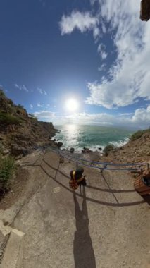 Dikey video. Mağara girişinden geniş açılı görüş açısı, bir adamın okyanus manzarasının tadını çıkarmak için korkuluklara doğru yürüdüğünü gösteriyor..