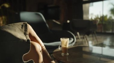 Güneş ışığı şık bir odadan geçer, mermer bir masanın üzerindeki latte bardağını aydınlatır ve bir kadının bacak bacak üstüne atarak sıcak ve huzurlu bir ortam yaratır..