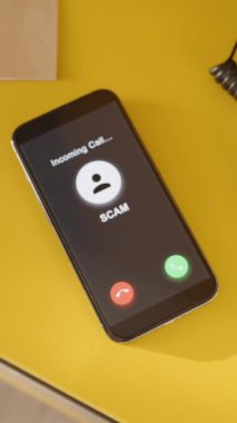 Dikey video. Bir kadın dolandırıcılardan gelen bir telefonla uyanır ve telefonu kapatır. Parlak sarı bir komodindeki akıllı bir telefon, dijital uyarı ve tetikte olduğunu gösteren, yeni ve minimalist bir yatak odası ayarında gelen bir dümen çağrısı sergiliyor..