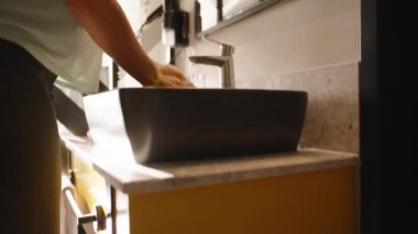 Çağdaş bir banyo ortamında temizlik ve temizliği vurgulayan, parlak siyah bir lavaboda ellerini yıkayan bir kadının yakın çekimi..
