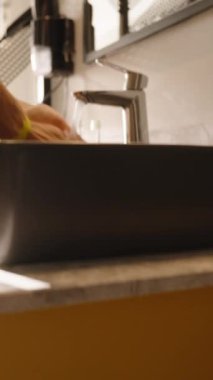 Dikey video. Çağdaş bir banyo ortamında temizlik ve temizliği vurgulayan, parlak siyah bir lavaboda ellerini yıkayan bir kadının yakın çekimi..