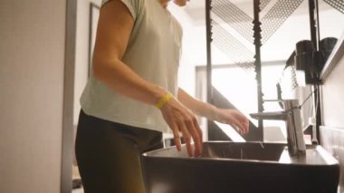 Bir kadın ellerini siyah bir lavabonun yanında beyaz bir havluyla kurular. Yumuşak doğal ışıkla aydınlatılmış temiz ve modern bir banyo sahnesini yakalar..