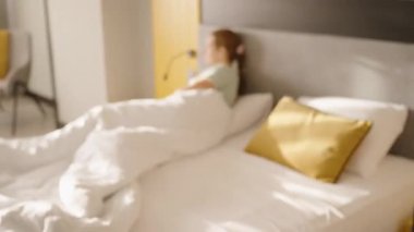 Beyaz yatağa sarılı bir kadın, telefonda konuşuyor. Sarı dekorlu, rahat ve rahat bir sabah geçiriyor..