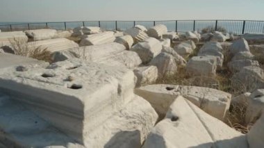 Parlak mavi gökyüzünün altında denize bakan korkulukların yanındaki tarihi kalıntılar, dağınık antik mermer bloklardan oluşan bir koleksiyon..