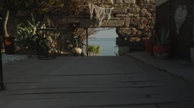 Antik bir duvarda dar bir taş kemer, saksı bitkileri ve yumuşak güneş ışığı altında kırsal dekorla çevrili sakin bir denizi çerçeveler..