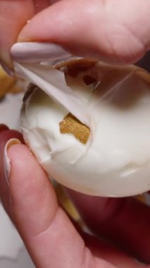 Dikey video. Haşlanmış bir Paskalya yumurtasını altın parçalarla soyan eller, altındaki beyaz yumurtayı ortaya çıkarıyor, kırık kabuk parçalarından oluşan bir zemin üzerine kuruluyor. yavaş çekim