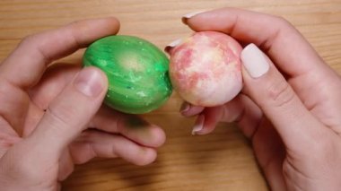 Erkek ve kadın eli Paskalya yumurtalarını tutarken birbirlerine vuruyorlar, onları ahşap bir masaya koyuyorum ve yavaş çekimde yuvarlanıyorlar.