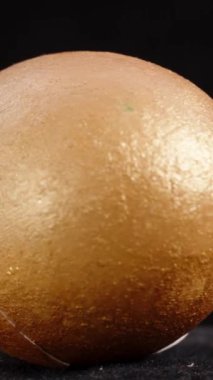 Dikey video. Çatlak bir yüzeyi olan tek bir altın Paskalya yumurtası, koyu bir zemin üzerine kurulmuş, dokulu ve parlak sonunu vurguluyor. döngü döndürmesi