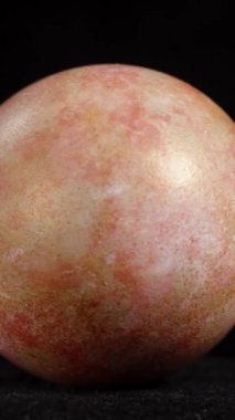 Dikey video. Tek bir mermer Paskalya yumurtası, ince pembe ve altın renkli, koyu bir arka plan üzerine kurulmuş, hassas desenlerini vurguluyor. döngü döndürmesi.