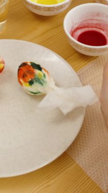 Dikey video. Paskalya kutlaması için hazırlanmış yumurta ve tabaklar dolusu boyayla süslenmiş bir Paskalya yumurtası..