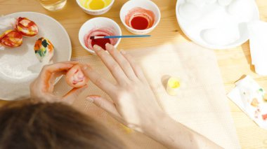 Bir kadın, bir masa boyası ve sarılı yumurtalarla Paskalya Yumurtası 'nı dikkatle resmediyor..