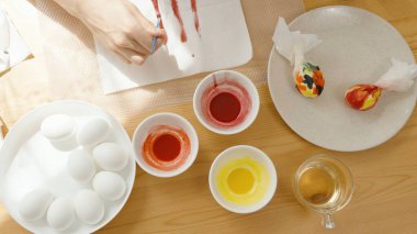 A Top-Down View of a Table with White Eggs, Bowls of Dye, and a Woman Painting for Easter. clipart