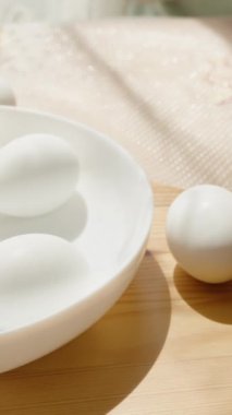 Dikey video. Paskalya yumurtalarını hazırlayan, boyalar ve beyaz yumurtalarla çevrili bir paspasın üzerine tasarımlar çizen kadın..