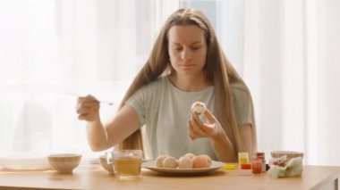 Paskalya yumurtasını parlak, güneşli bir odada boyama malzemeleri ve pastel renkli yumurtalarla süsleyen odaklanmış bir kadın..