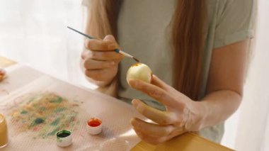 Paskalya yumurtasını farklı renklerde boyayan bir kadın. Çalışma odasını aydınlatan güneş ışığı..